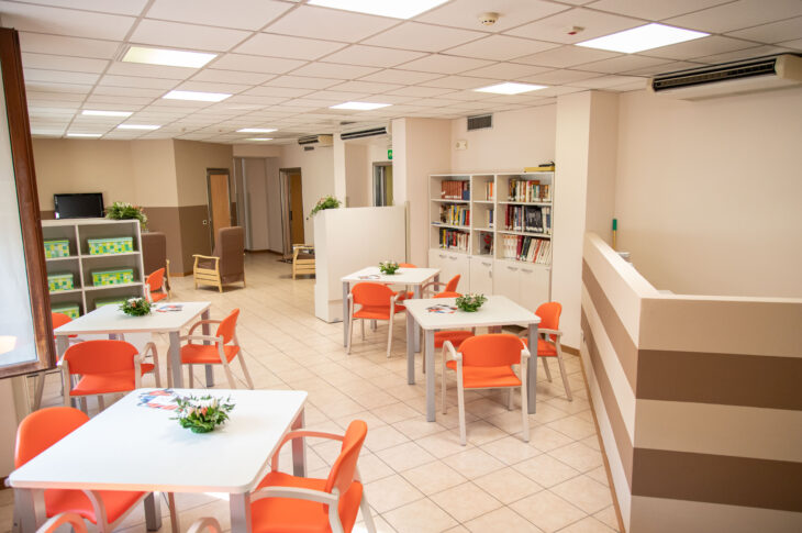Sala comune con tavoli, sedute, libreria e area relax.