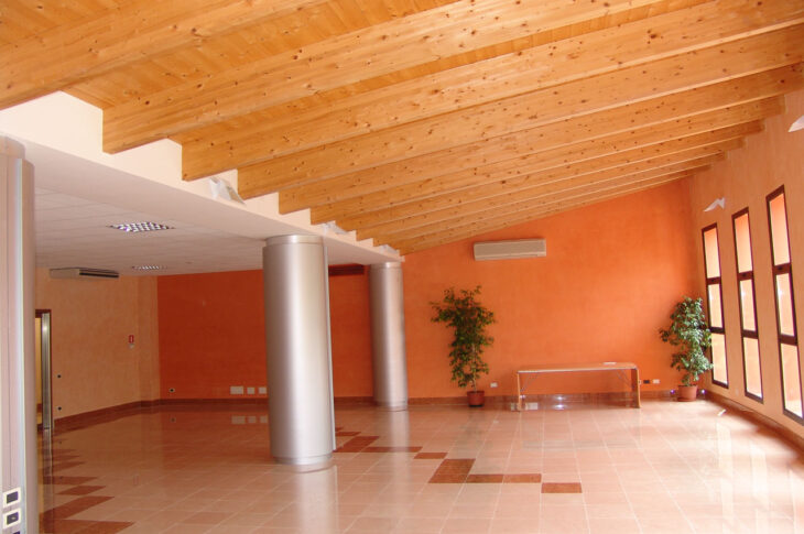 Sala polivalente con ampio spazio, colonne centrali e grandi finestre.