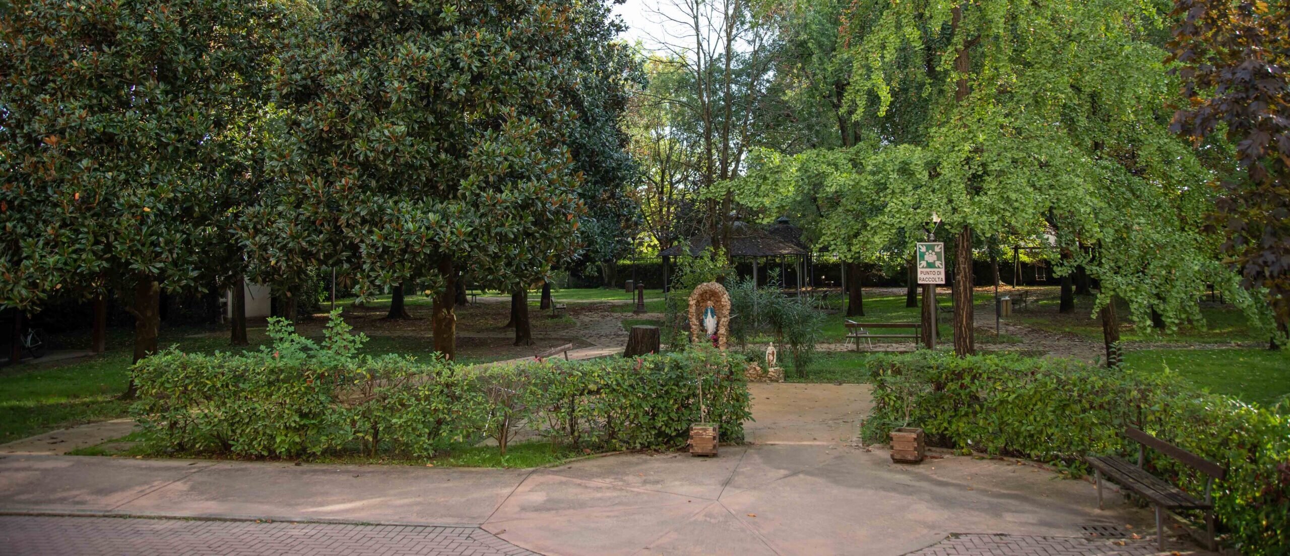 Giardino dell'ente con grandi alberi, sentieri pavimentati, panchine, gazebo e aree verdi accessibili.
