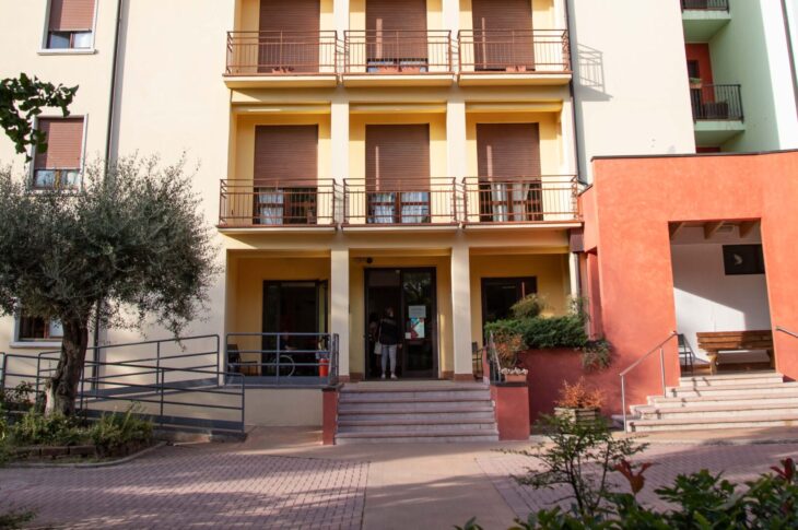 Ingresso principale della Casa di Riposo Benedetto Albertini, con edificio multipiano dotato di balconi, rampa di accesso, scale, area pavimentata e spazi verdi antistanti.